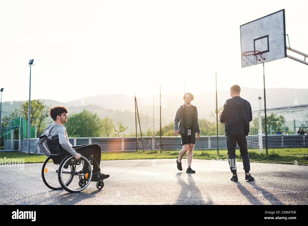 Behinderter junger Mann im Rollstuhl, der mit seinen Freunden Basketball spielt. Teamwrok und männliche Freundschaft. Stockfoto