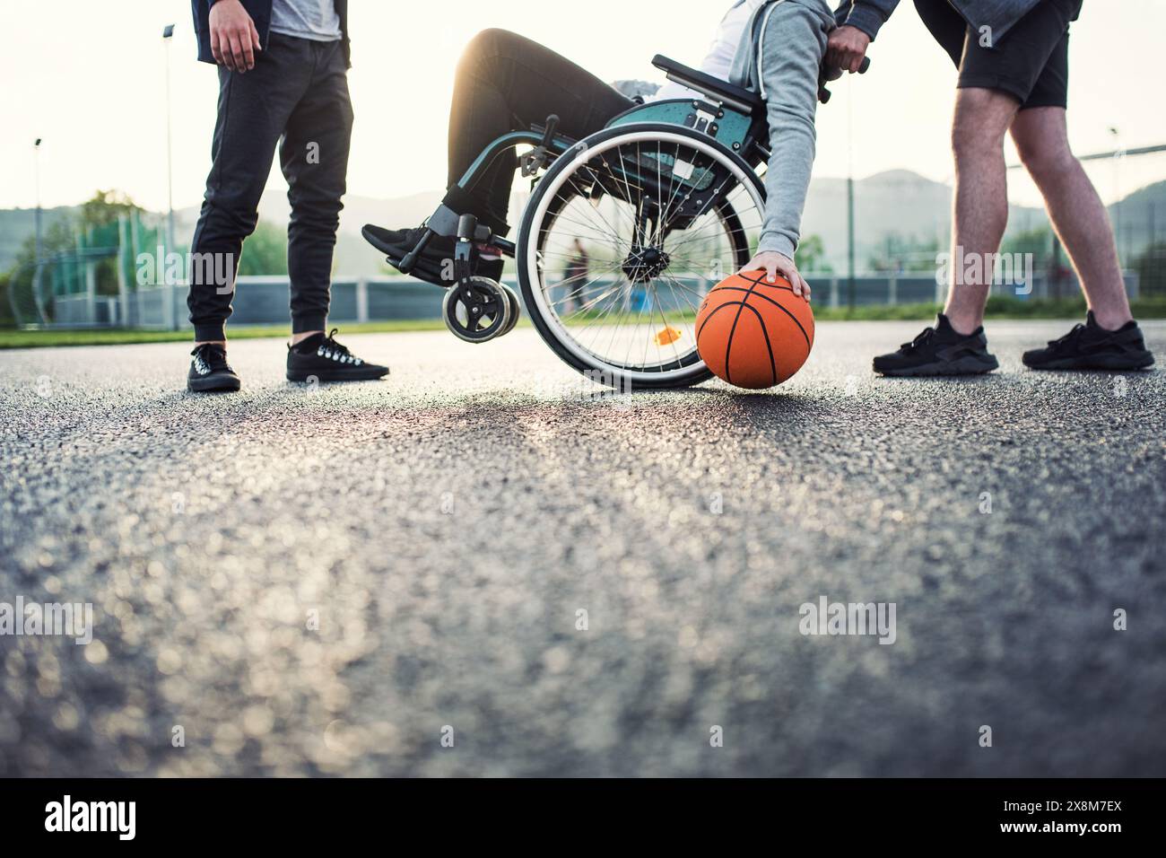 Behinderter junger Mann im Rollstuhl, der mit seinen Freunden Basketball spielt. Teamwrok und männliche Freundschaft. Stockfoto