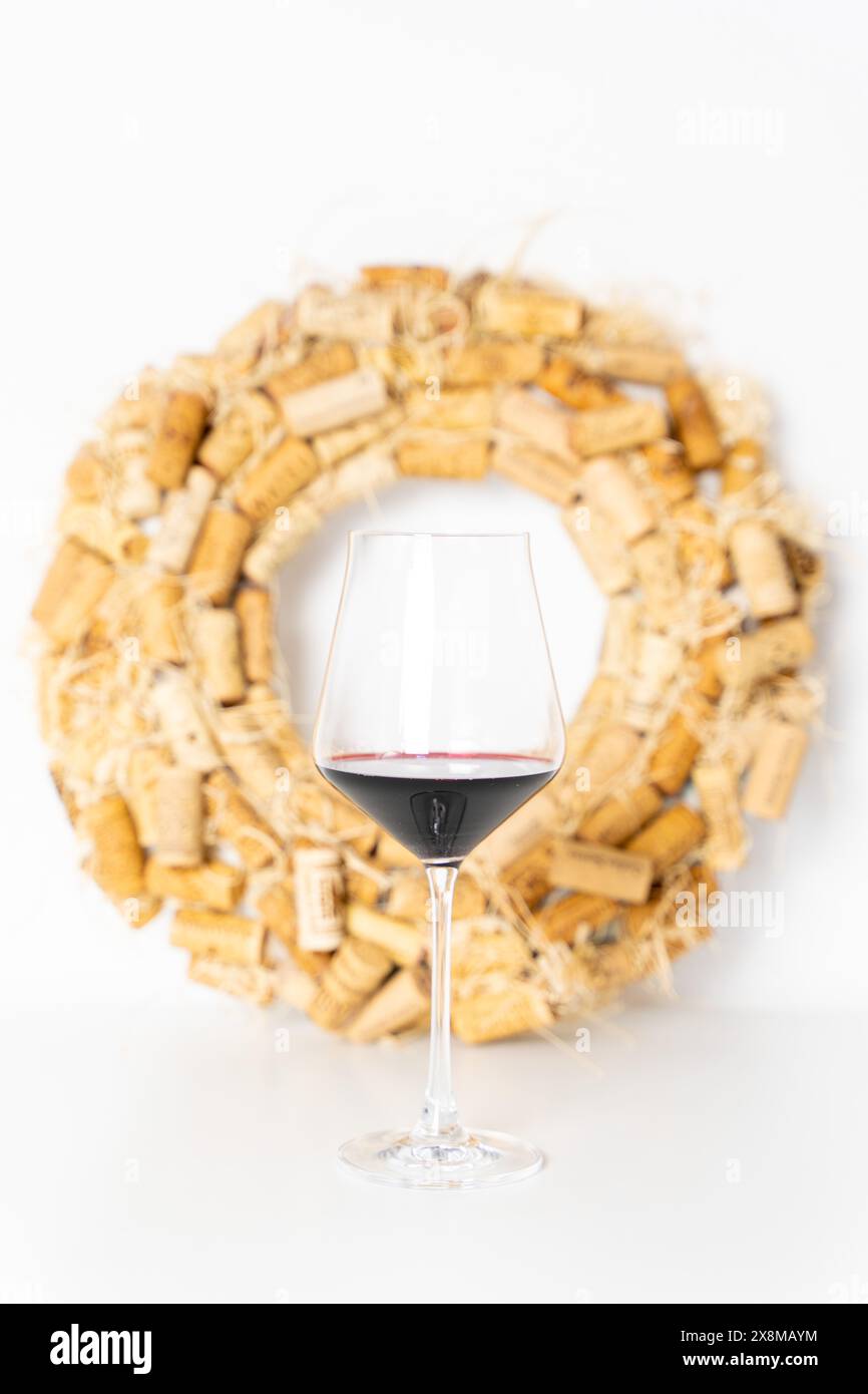 Ein Glas Rotwein auf einem weißen Tisch, vor dem Hintergrund eines Kranzes aus Weinkorken. Ausgewählter Fokus. Hochwertige Fotos Stockfoto