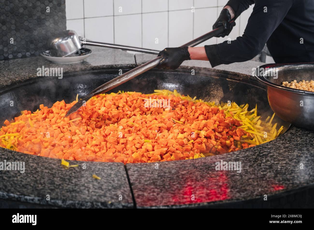 Der männliche Koch rührt Karotten in einem Kessel, um traditionelle usbekische Pilaw in der Küche eines Restaurants in Usbekistan zu kochen Stockfoto