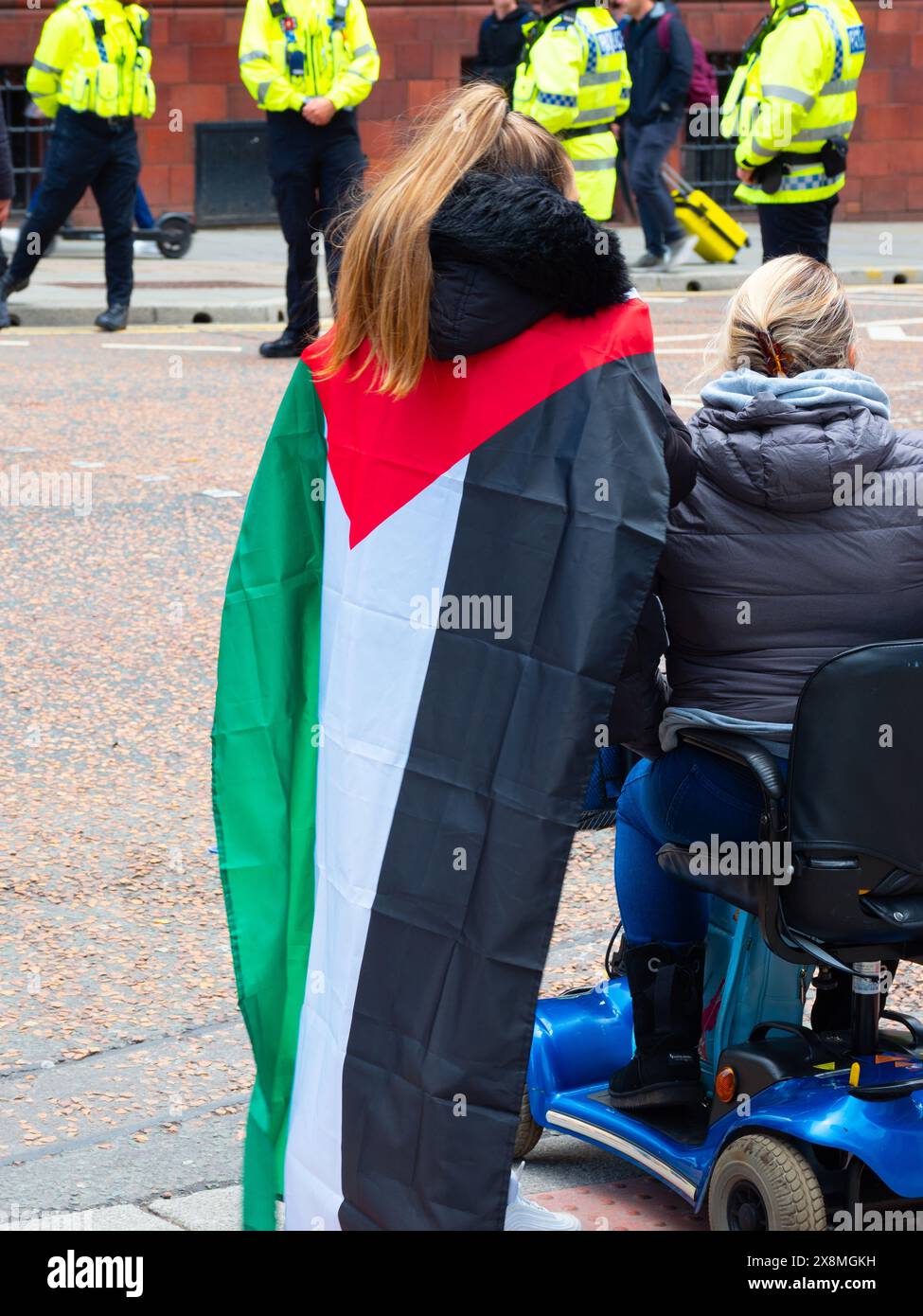 Manchester UK 26. Mai 2024. Zwei Frauen protestieren, eine mit palästinensischer Flagge, mit Polizisten im Hintergrund. Stockfoto