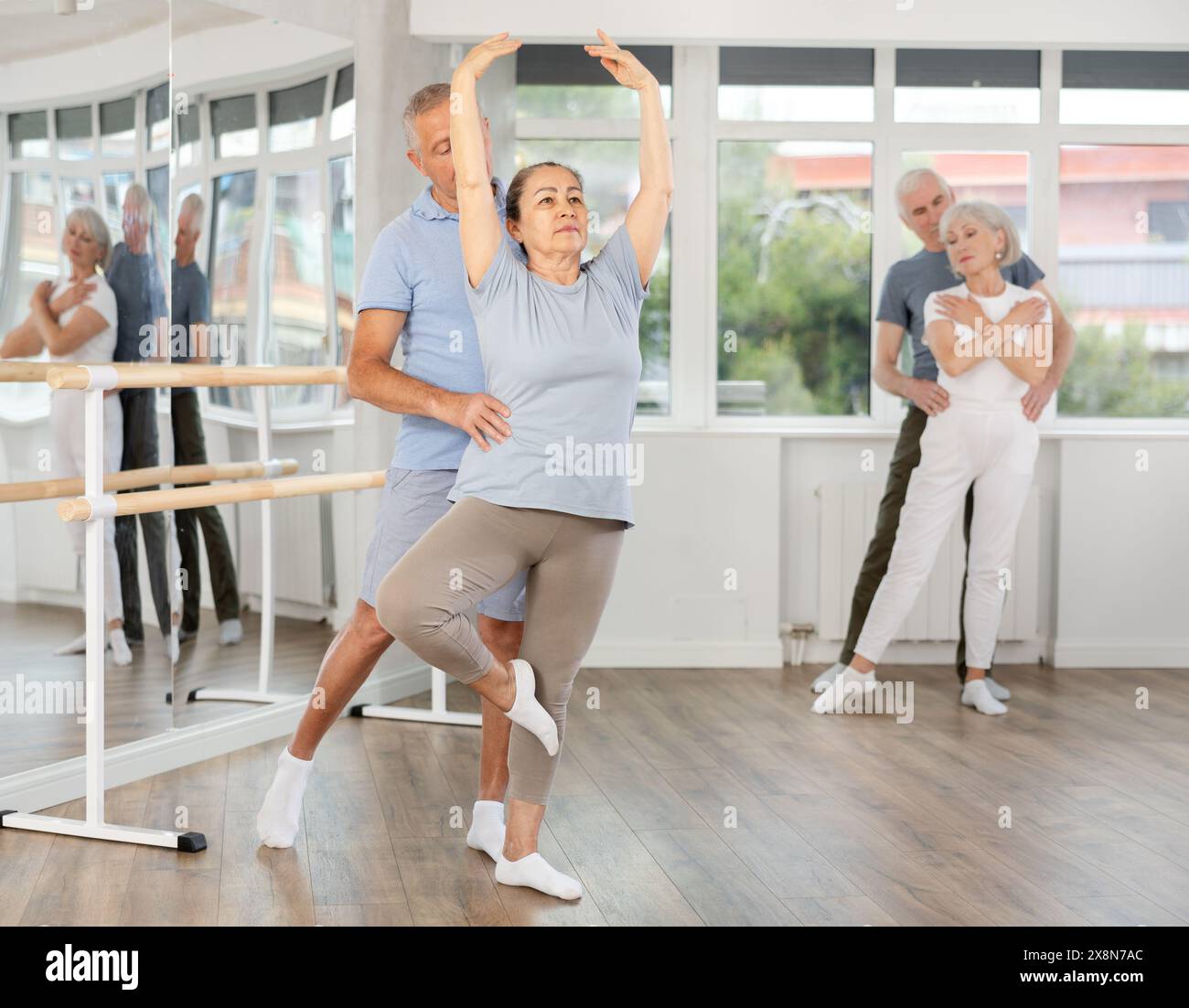 Glückliche, reife Balletttänzer zeigen Choreographie mit Unterstützung während der Gruppenschulungen im Tanzstudio Stockfoto