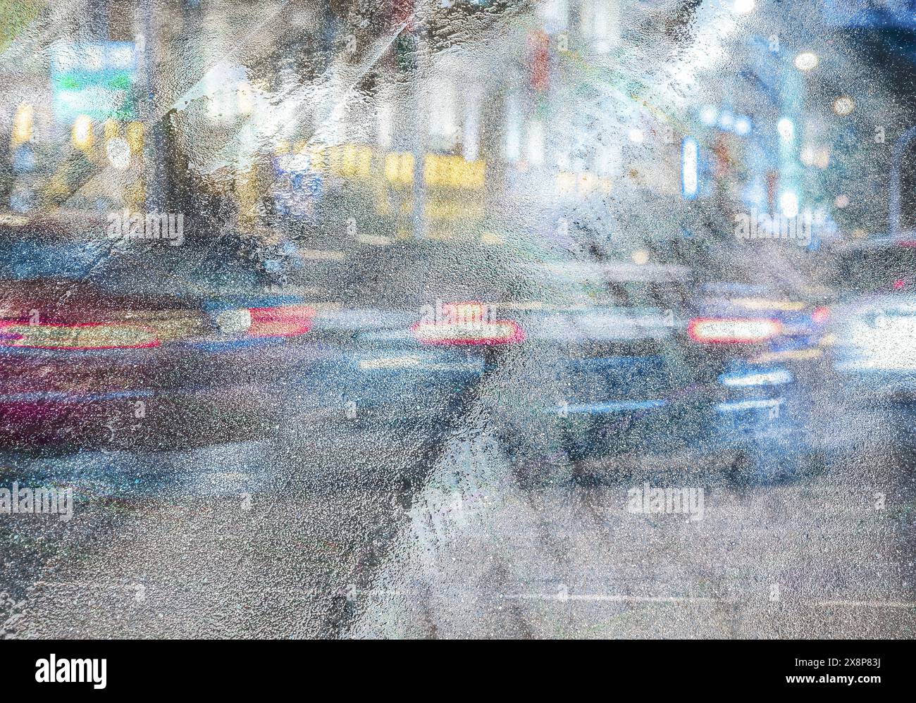 Nasse Asphaltstraße mit Stadtverkehr und Straßenlaternen. Mehrfach belichtetes Stadtbild bei regnerischer Nacht. Stockfoto