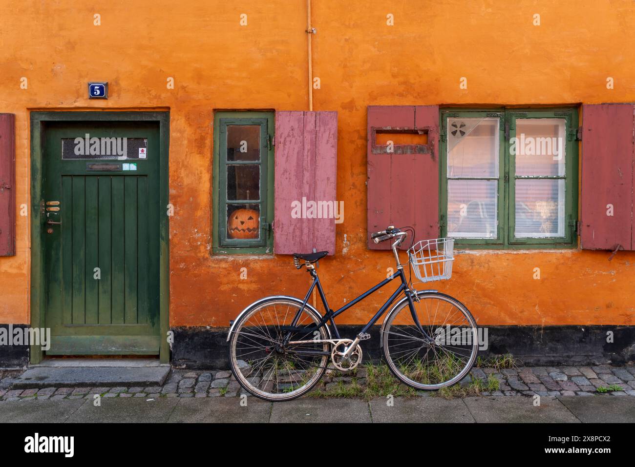 In diesem Bild erwacht eine malerische europäische Straße zum Leben, in der sich ein Vintage-Fahrrad mit einem Korb an eine orangene Wand lehnt Stockfoto