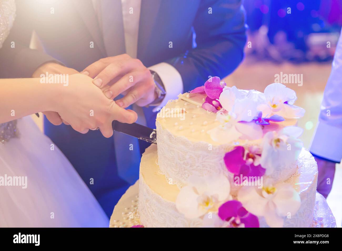 Glückliche Braut und Bräutigam schneiden Hochzeitstorte dekoriert mit roten Rosenblumen im Restaurant, Kopierraum. Hochzeitsfeier Stockfoto