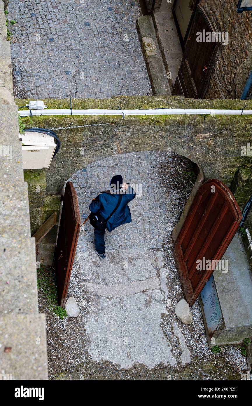 Person, die durch einen offenen Bogengang in Carcassonne geht, von oben erfasst und die mittelalterlichen Mauerwerke und kopfsteingepflasterten Pfade hervorhebt. Stockfoto