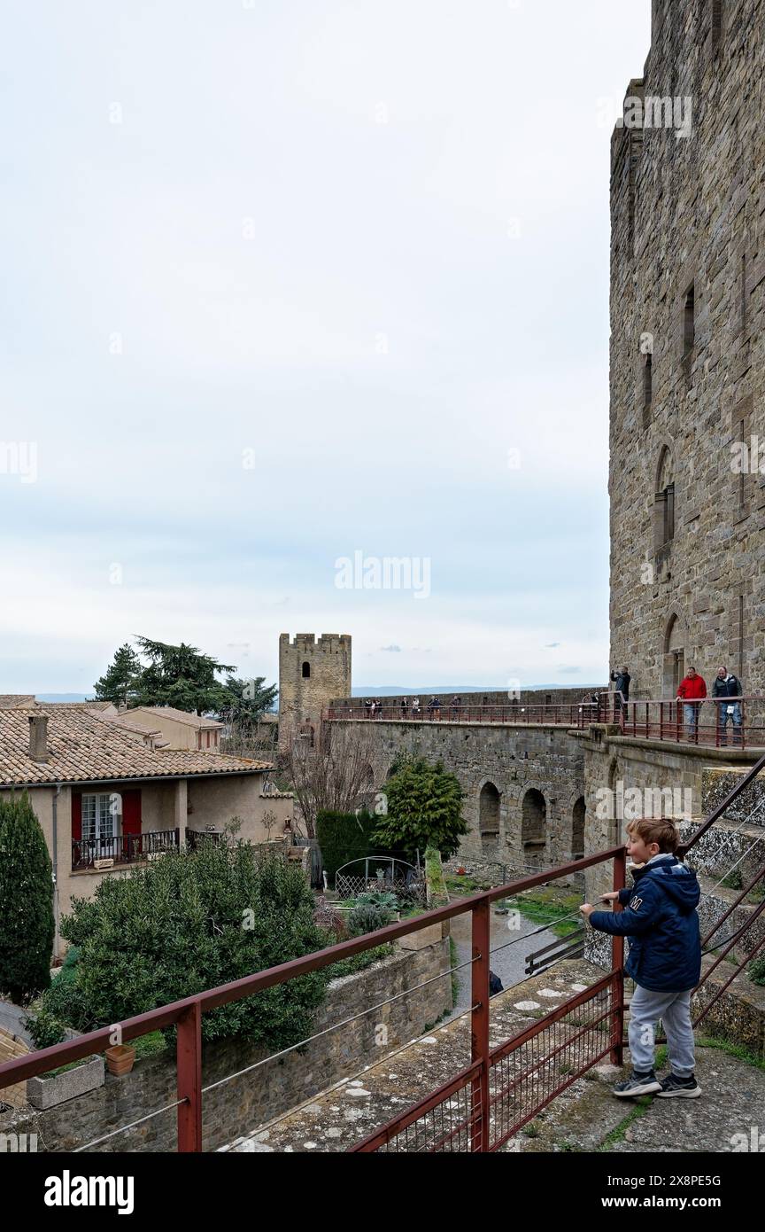 Kind steht auf den Stadtmauern von Carcassonne, mit Blick auf historische Steinbauten und Innenhöfe, mit mittelalterlichen Türmen im Hintergrund. Stockfoto