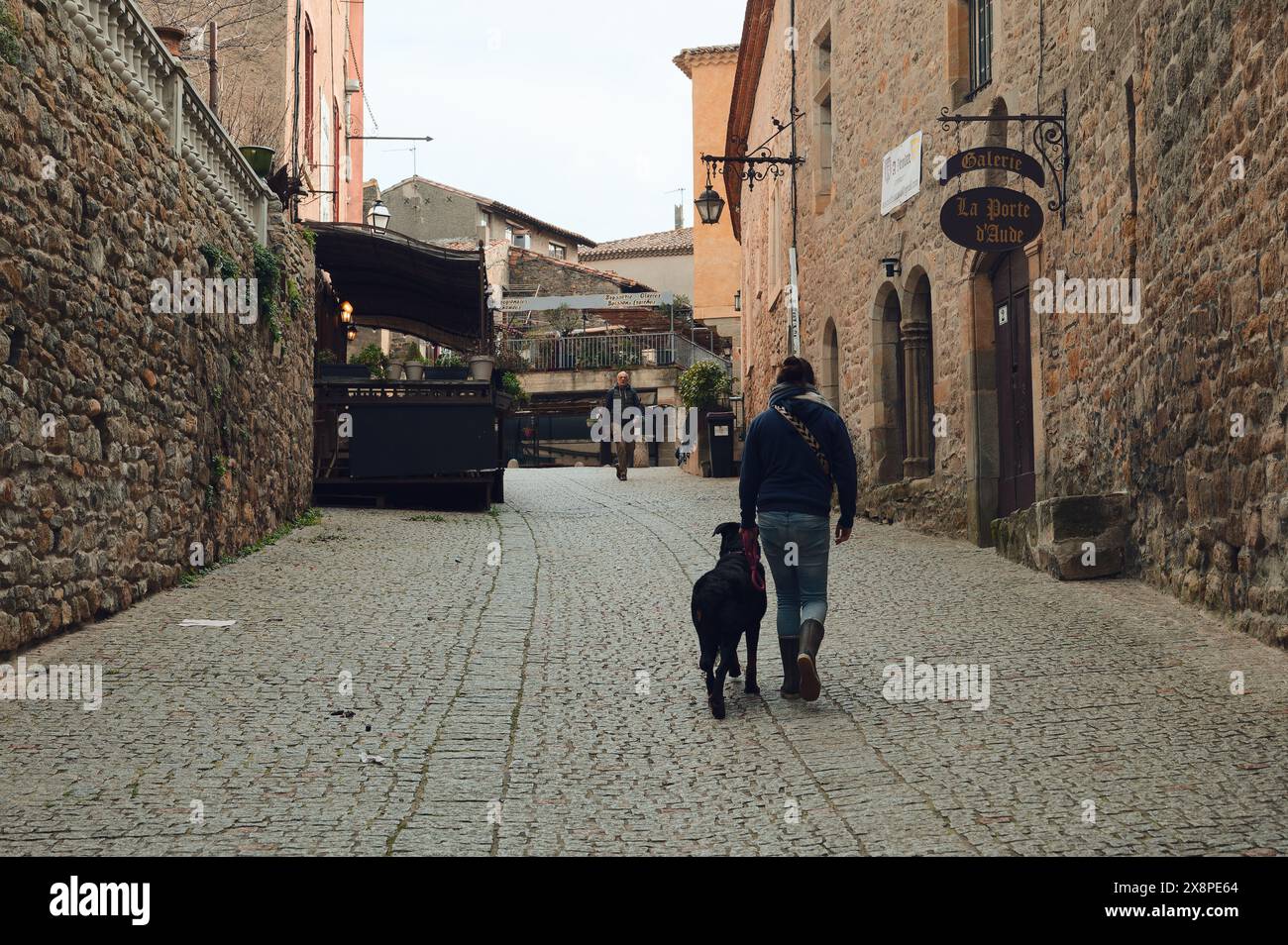 Eine Person und ein Hund gehen auf einem Kopfsteinpflasterweg. Flankiert von historischen Steinhäusern in dieser rustikalen mittelalterlichen Straße. Stockfoto