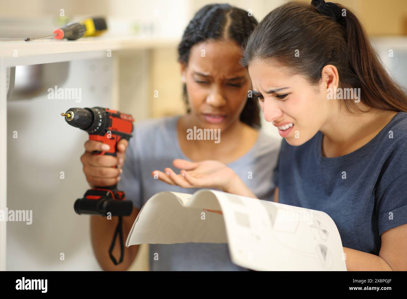 Zwei verwirrte Frauen, die das Haus reformieren, lesen in der Küche eine Anleitung für Möbel Stockfoto