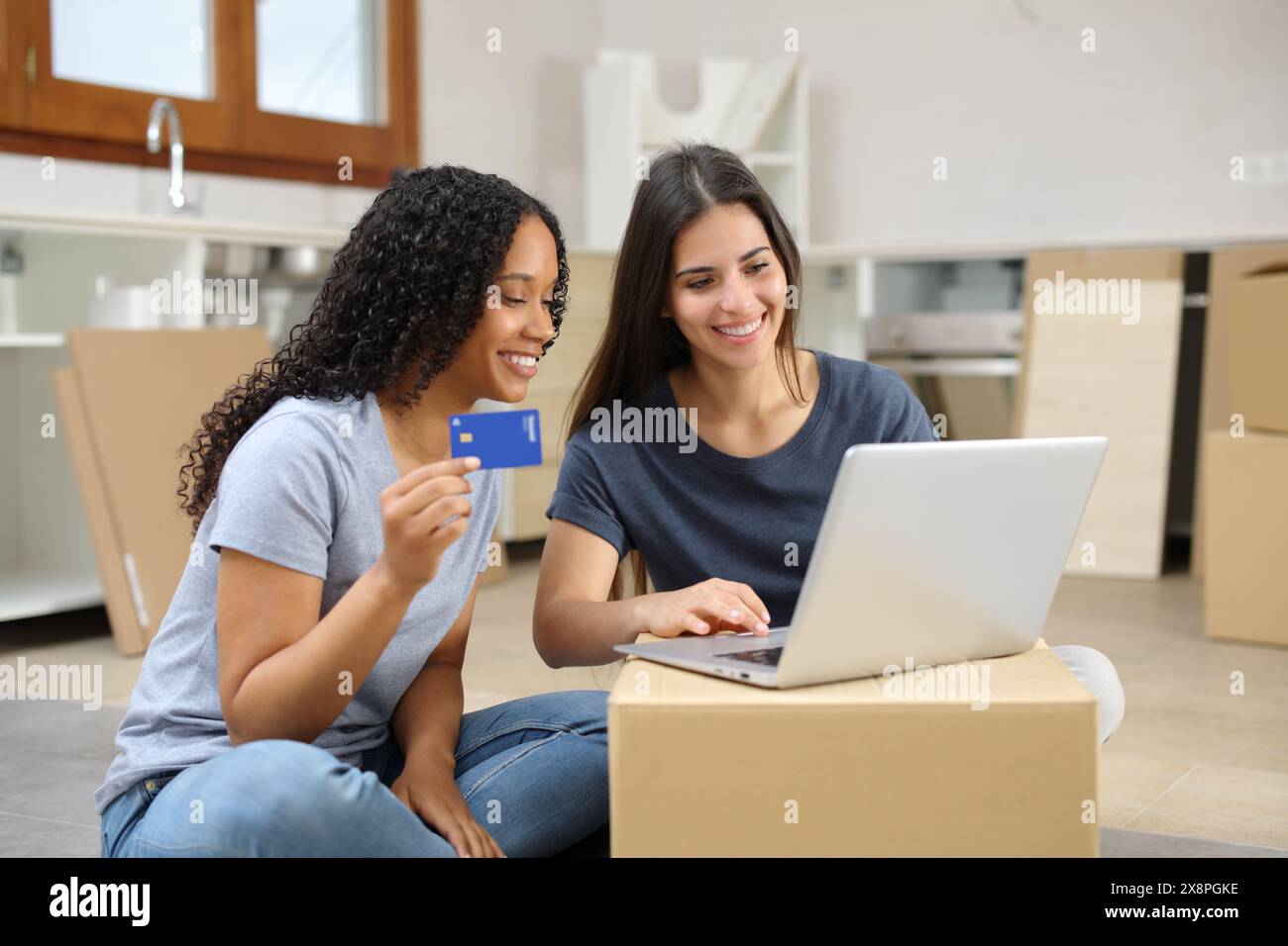 Zwei glückliche Mitbewohner ziehen nach Hause und kaufen online mit Laptop und Kreditkarte in der Küche Stockfoto