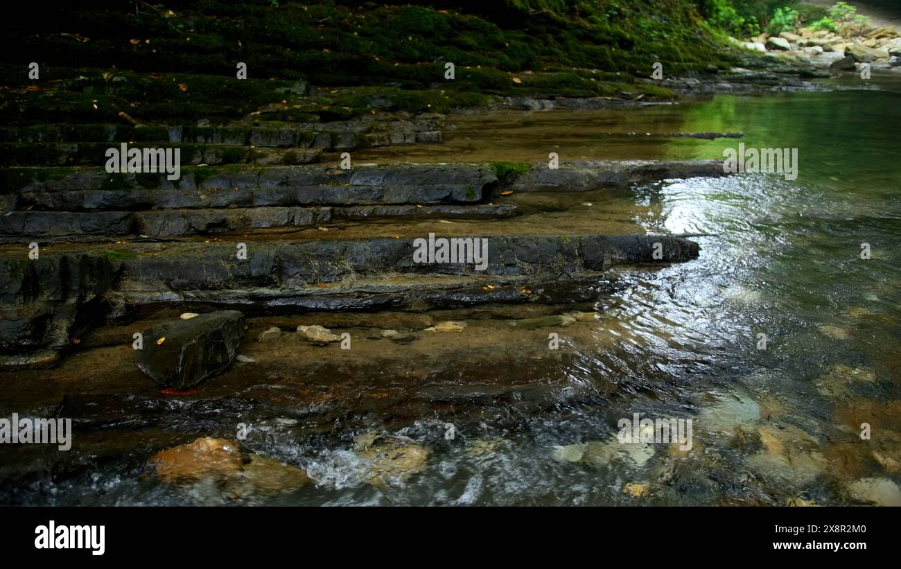 Klarer Bach, der durch Steinblöcke fließt. Kreativ. Ruhiger Fluss, der in Zeitlupe auf dem Steinboden fließt. Stockfoto