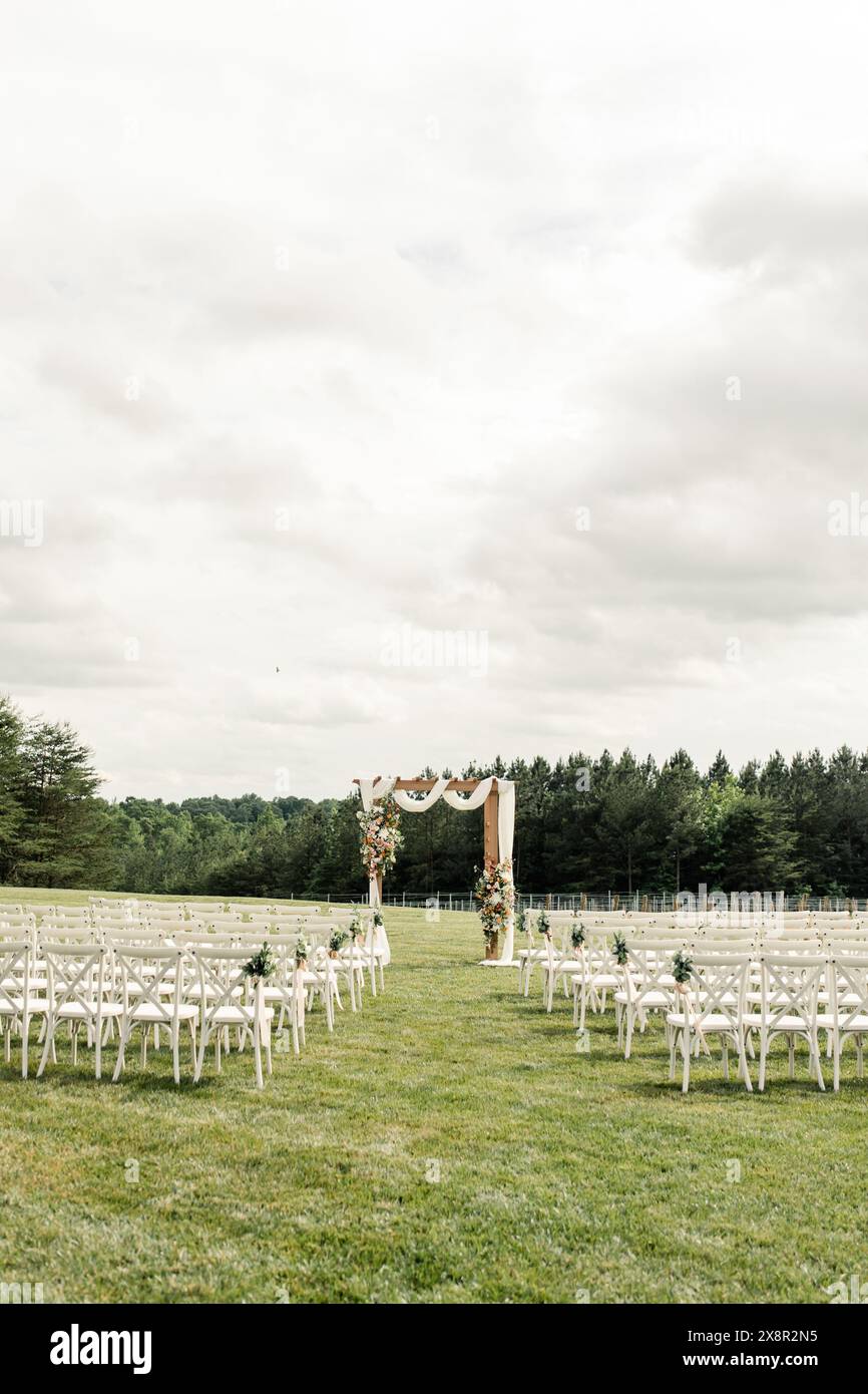 Hochzeitszeremonie im Freien mit Blumenbogen und Reihen weißer Stühle= Stockfoto