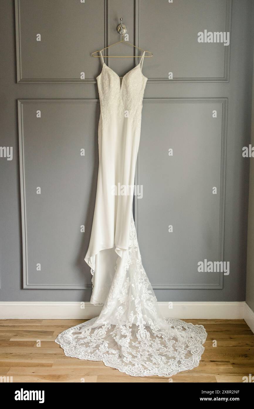 Weißes Hochzeitskleid mit Spitzendetails, die an einer grauen Wand hängen Stockfoto