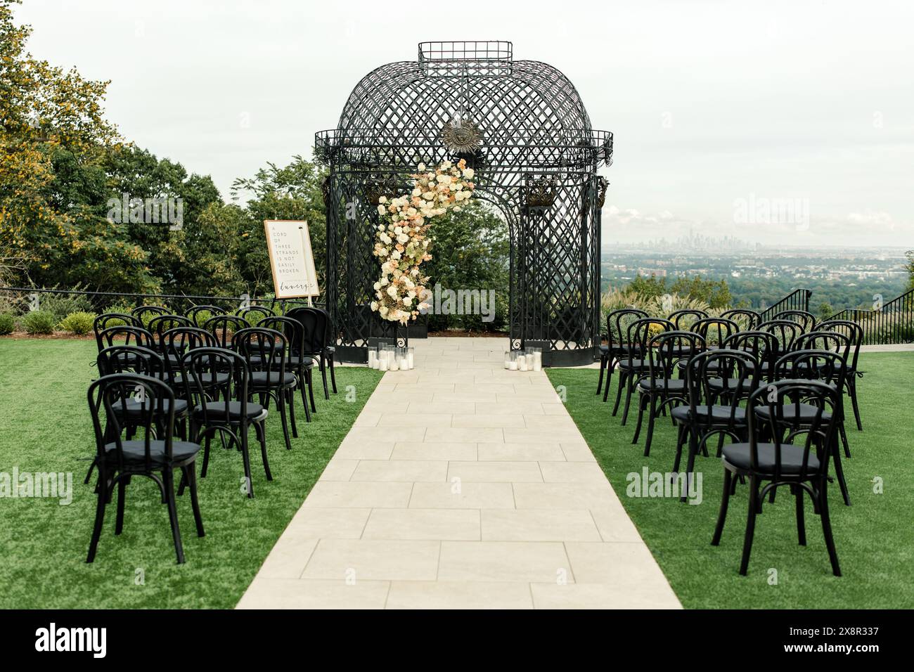 Hochzeitszeremonie im Freien mit schwarzen Stühlen und einem Blumenbogen aus Metall Stockfoto