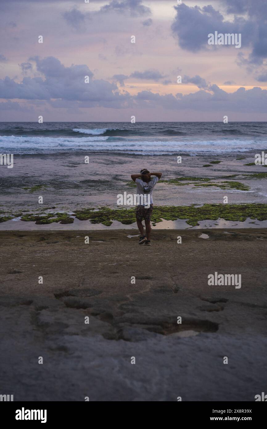 Ein Mann mit Kopfhörern hört Musik am Strand in der Nähe des Ozeans. Stockfoto