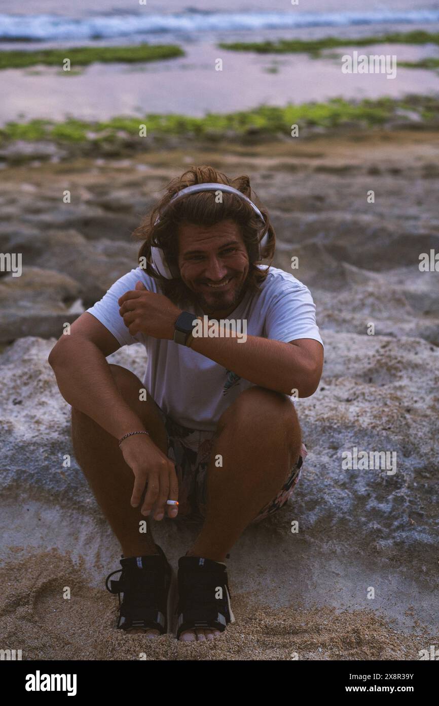 Ein Mann mit Kopfhörern hört Musik am Strand in der Nähe des Ozeans. Stockfoto