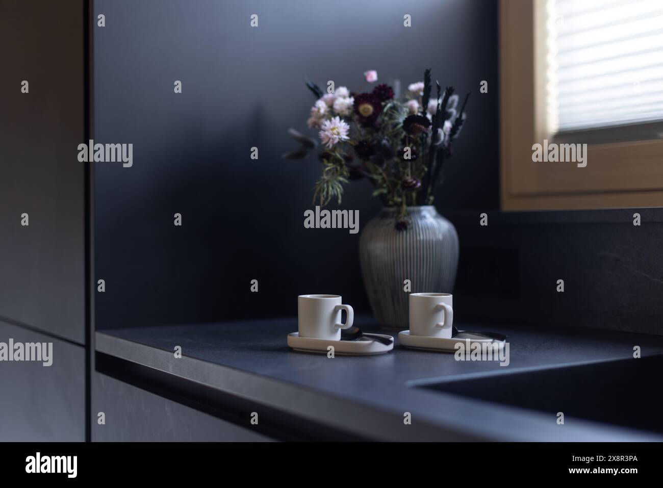 Schwarze Küchenecke mit Blumenstrauß und weißen Espresso-Tassen Stockfoto