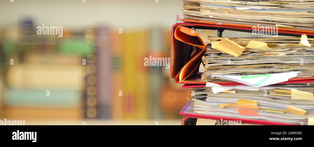 Stapel von unordentlichen Aktenordnern mit geringer Schärfentiefe, verschwommenem Bücherregal auf der Rückseite, Bürokratie, Aminisierung, Geschäftskonzept. Stockfoto