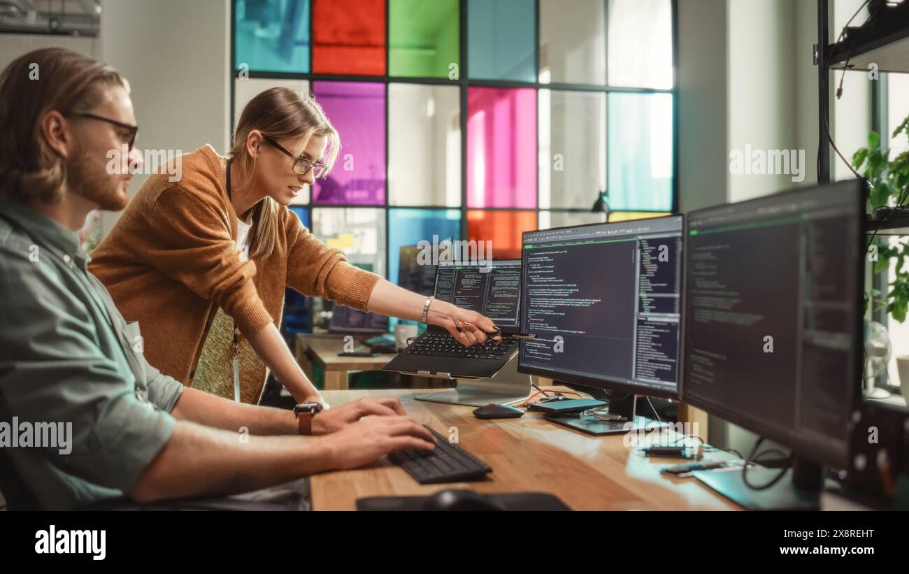 Weibliche Senior Software Engineer berät männliche Junior Developer und zeigt auf Desktop Computer Display mit Code. Kaukasische Frau bietet neue Funktionen und hilft bei der Behebung von Fehlern in der modernen SaaS-Plattform. Stockfoto