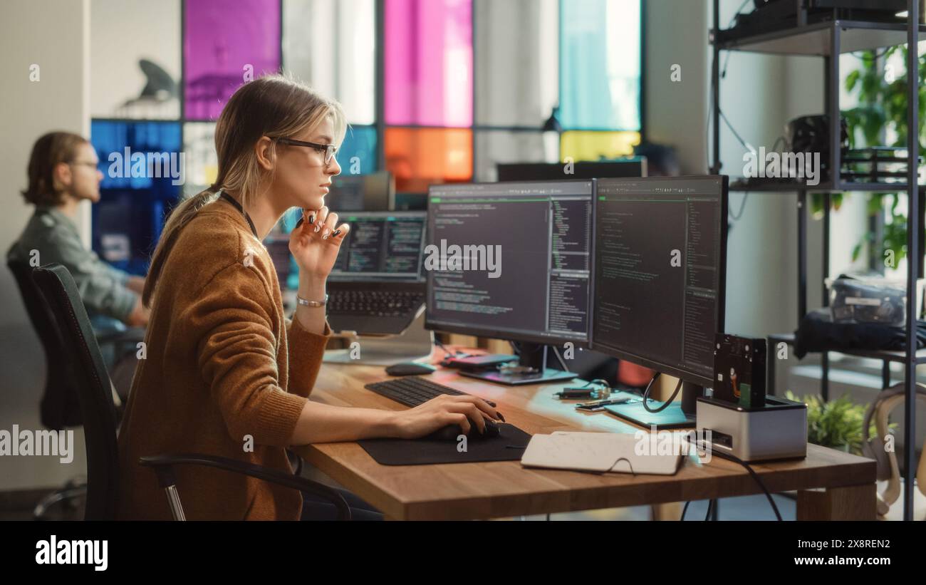 Die weiße Frau schreibt Codezeilen auf einem Desktop-PC mit mehreren Displays und einem Laptop im eleganten Büro. Professionelle Datenwissenschaftlerin mit Software zur Analyse von Informationen aus dem Internet. Stockfoto