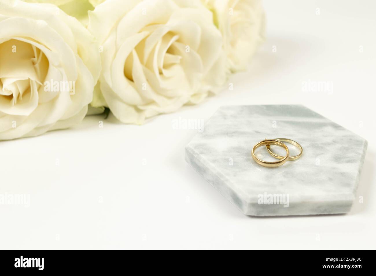 Weiße Rosen und goldene Eheringe auf weißem Hintergrund. Hochzeitskomposition, Marmortablett, Podium. Kopierraum, flach. Stockfoto