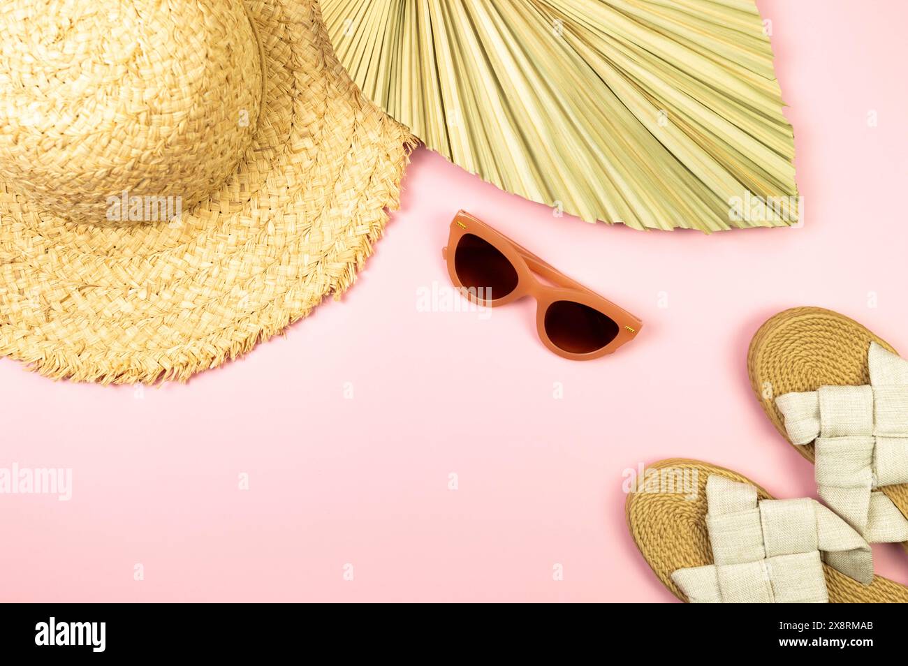 Blick von oben auf Strohhut, getrocknete Palmblätter, Hausschuhe und Sonnenbrille auf rosafarbenem Hintergrund. Sommermode, Urlaubs- und Strandtapete. Kopierraum, flach. Stockfoto