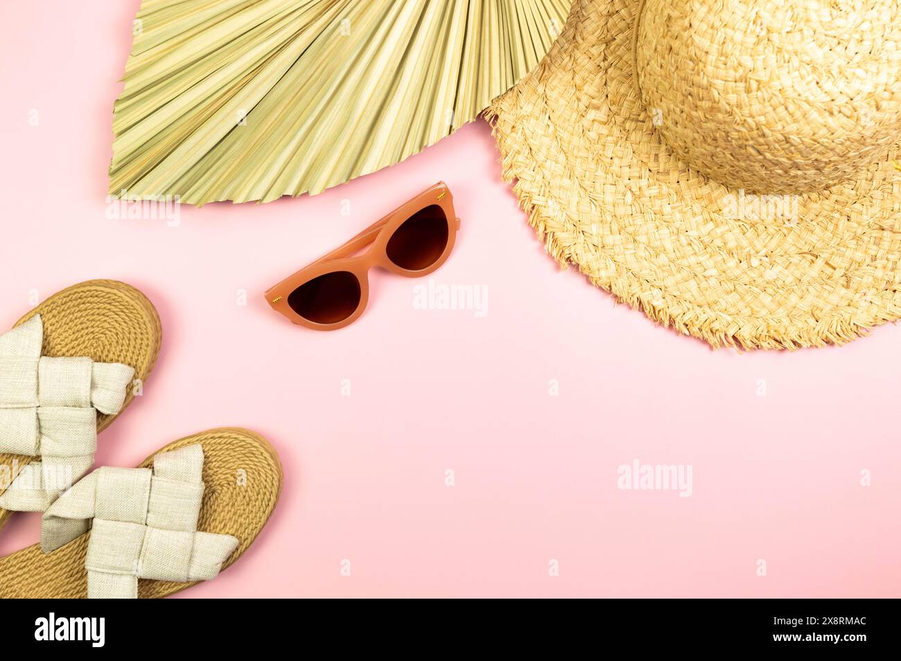 Blick von oben auf Strohhut, getrocknete Palmblätter, Hausschuhe und Sonnenbrille auf rosafarbenem Hintergrund. Sommermode, Urlaubs- und Strandtapete. Kopierraum, flach. Stockfoto