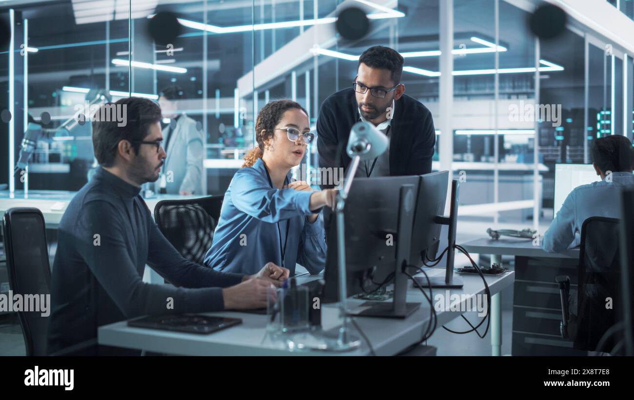 Ein Team innovativer Industrieingenieure bespricht mithilfe des Computers ein technologisches Projekt im modernen Fabrikbüro Industrie 4,0. Gruppe von Wissenschaftlern arbeitet im Forschungs- und Entwicklungszentrum. Stockfoto