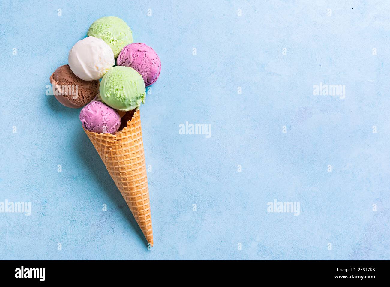 Eisbecher mit verschiedenen Schaufeln auf blauem Hintergrund, kreative Sommerflachlage, Kopierraum. Viele bunten Bio-Eiskugeln in Waffelkegel. Stockfoto