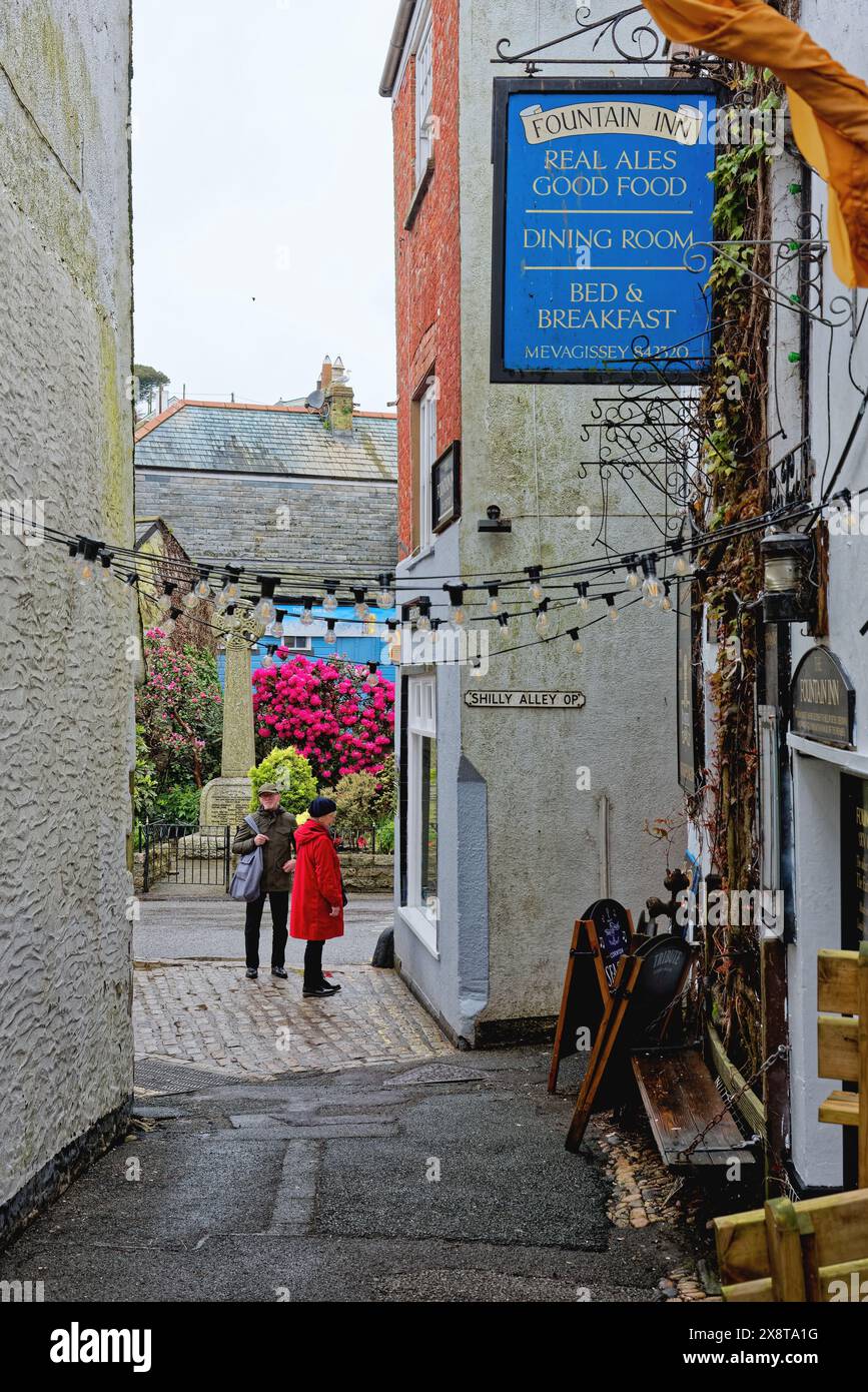 Zwei Touristen in der engen Cliff Street mit dem Eingang zum Fountain Inn, Mevagissey Cornwall England, Großbritannien Stockfoto