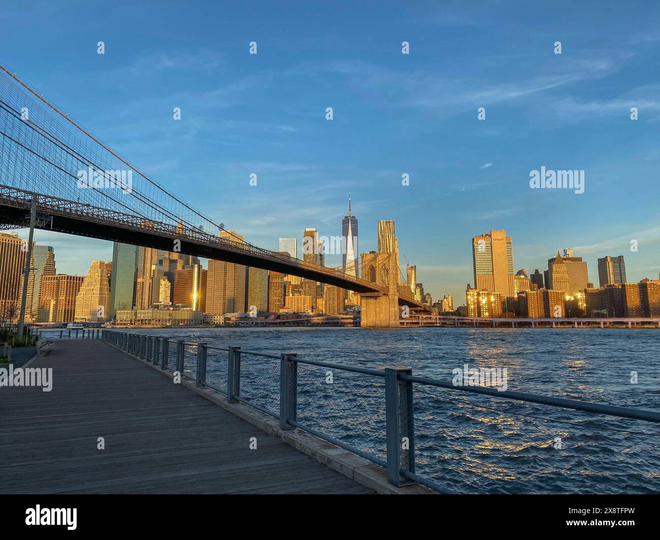 Malerischer Blick über die Brücke und die Stadt im Abendlicht, reflektiert im Wasser, große Brücke über einen Fluss mit einer imposanten Skyline im Hintergrund Stockfoto