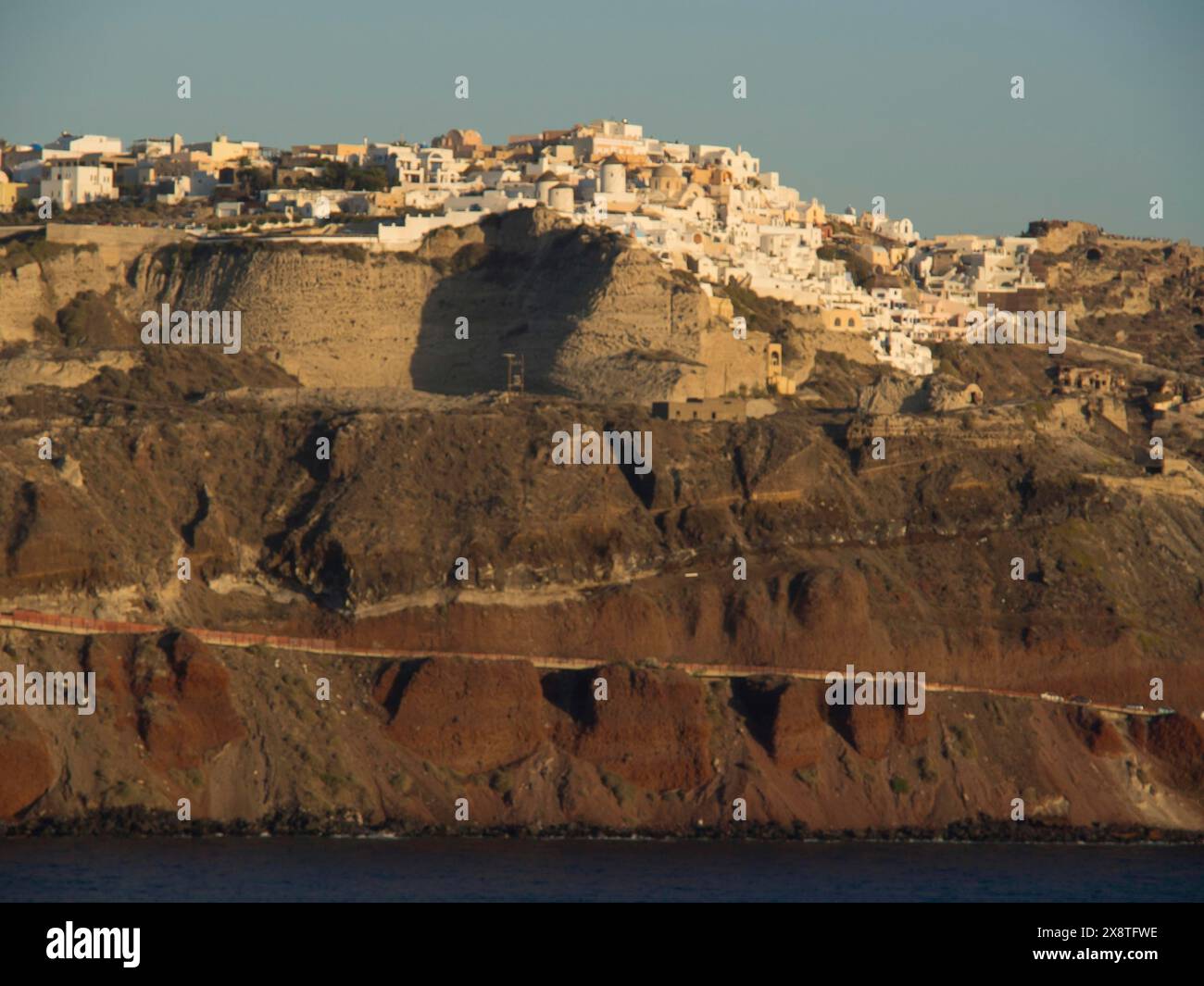 Ein Dorf mit weißen Gebäuden auf einer felsigen Klippe bei Sonnenuntergang, braune Vulkaninsel im blauen Meer mit weißen Häusern, Santorin, Griechenland Stockfoto