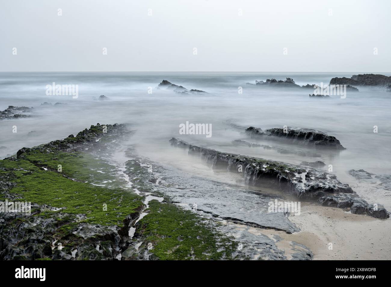 Eine ruhige Szene am Amoreira Beach in Portugal, mit nebelbedeckten Felsen und sanften Wellen, die sanft gegen die Sandküste schlagen. Die ruhige Atmosphäre Stockfoto