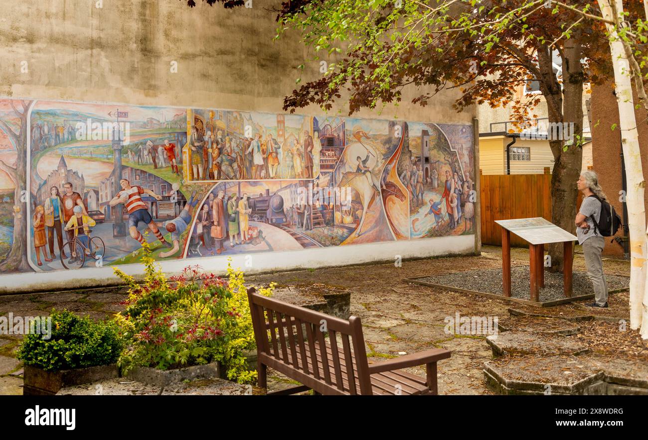 Ein Besucher bewundert ein Wandbild, das das Leben und die Zeit in der Stadt Peebles an der schottischen Grenze darstellt. Das Wandbild wurde von Michael Jessing gemalt. Stockfoto