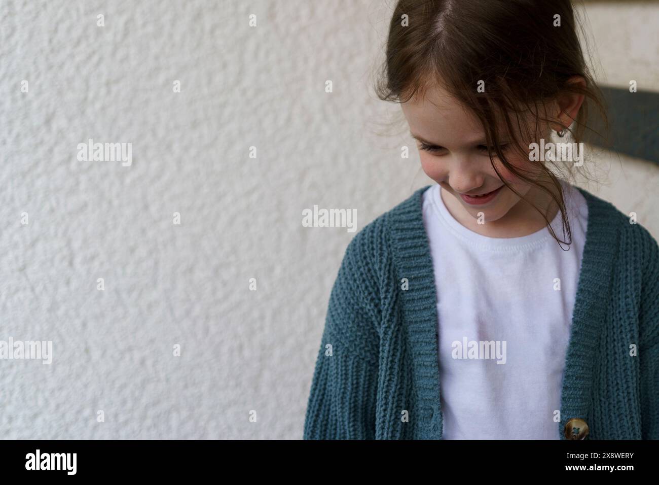 Ein lächelndes Mädchen in einem T-Shirt und einer Jacke steht am Eingang zum Haus Stockfoto