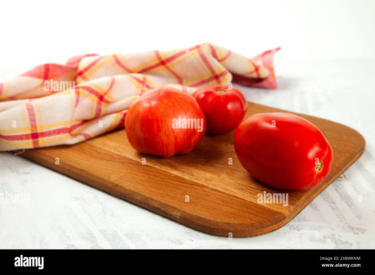 Hölzernes Schneidebrett mit mehreren verschiedenen Reifen saftigen Tomaten und rotem Küchentuch auf weißem hölzernem Hintergrund. Gemüsesammlung. Stockfoto