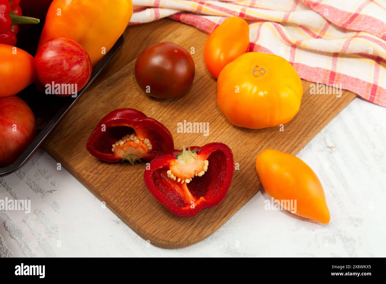 Schüssel mit Gemüse auf Schneidebrett mit verschiedenen ganzen Reifen saftigen Tomaten und Paprika auf weißem hölzernem Hintergrund mit roter Küche t Stockfoto