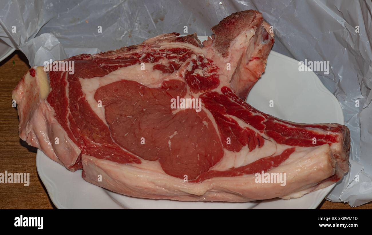 Ein erstklassiges Rohbeef-Steak, reich an Marmorierung und Farbe, präsentiert auf einem weißen Teller, bereit für die kulinarische Zubereitung Stockfoto