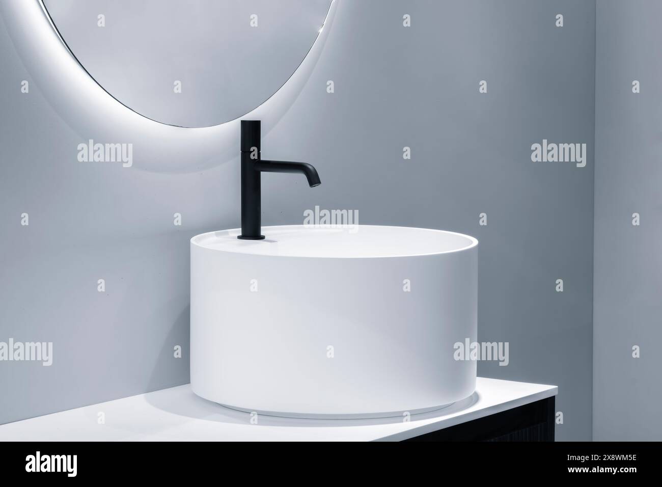 Ein weißes Waschbecken mit schwarzem Wasserhahn befindet sich im Badezimmer. Das Waschbecken ist rund und hat ein modernes Design. Das Bad ist sauber und gepflegt Stockfoto