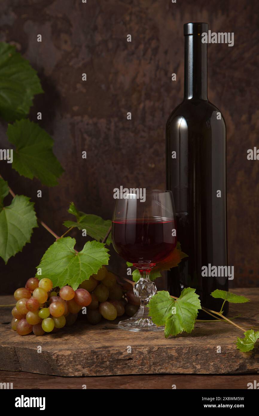 Das Konzept eines köstlichen alkoholischen Getränks, Wein und Trauben. Weinflasche, Glas Rotwein und Trauben auf dunklem rustikalem Holzhintergrund mit Stockfoto