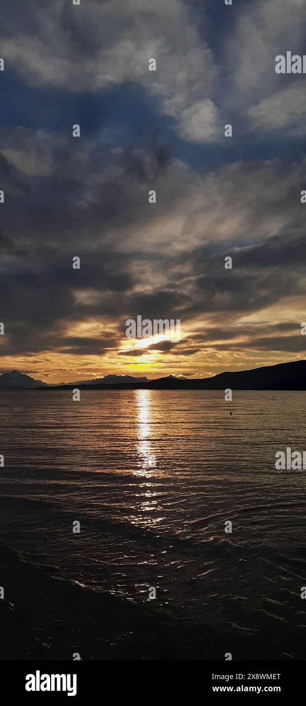 Dramatischer Sonnenuntergang über einem ruhigen Meer mit dunklen Wolken, die teilweise die Sonne verdecken und das Licht reflektiert auf dem Wasser Stockfoto