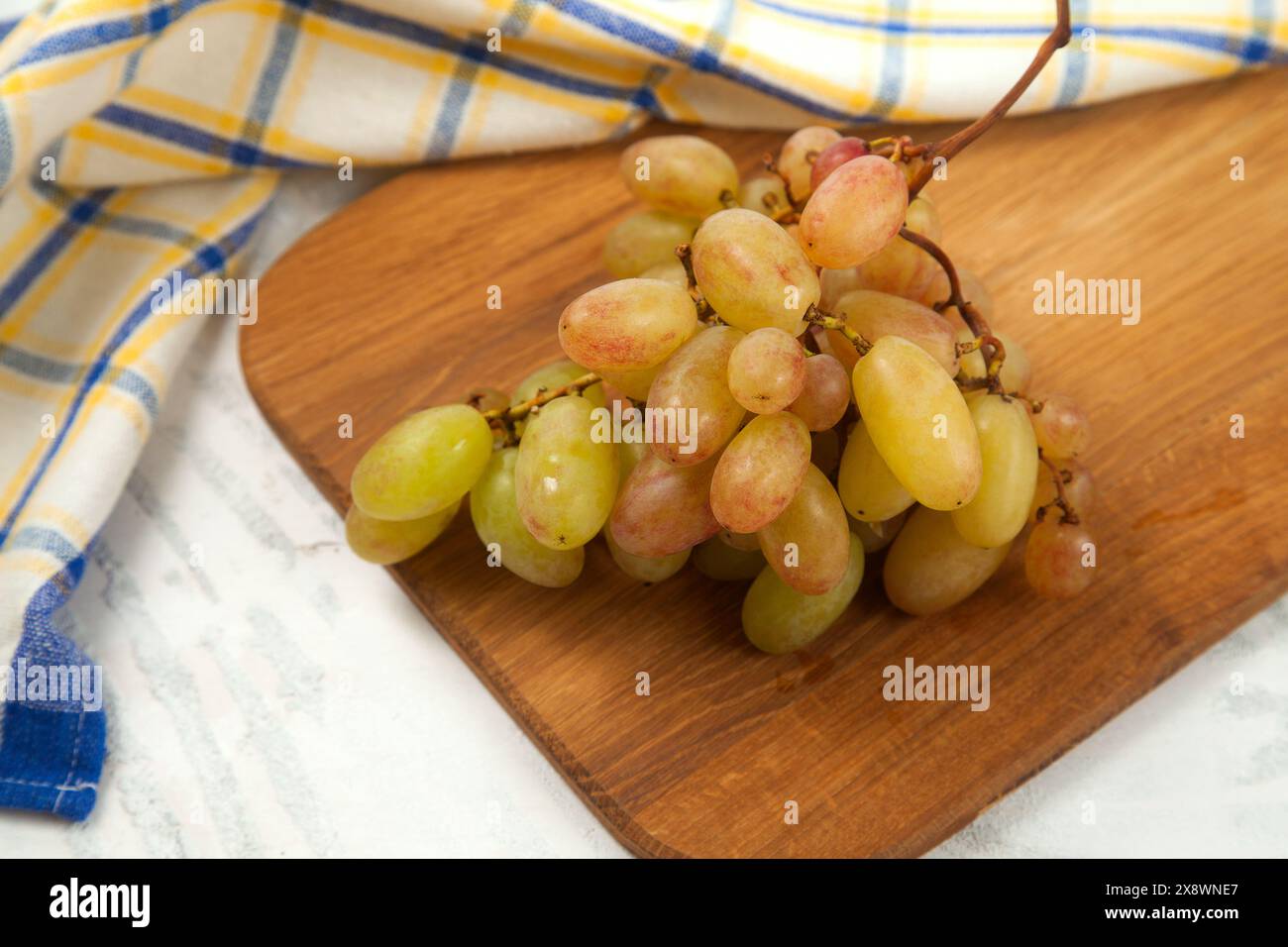 Schneidebrett mit einem großen Haufen reifer rosafarbener Trauben auf weiß. Rosafarbene Weintrauben mit blauem Küchentuch auf weißem hölzernem Hintergrund. Stockfoto