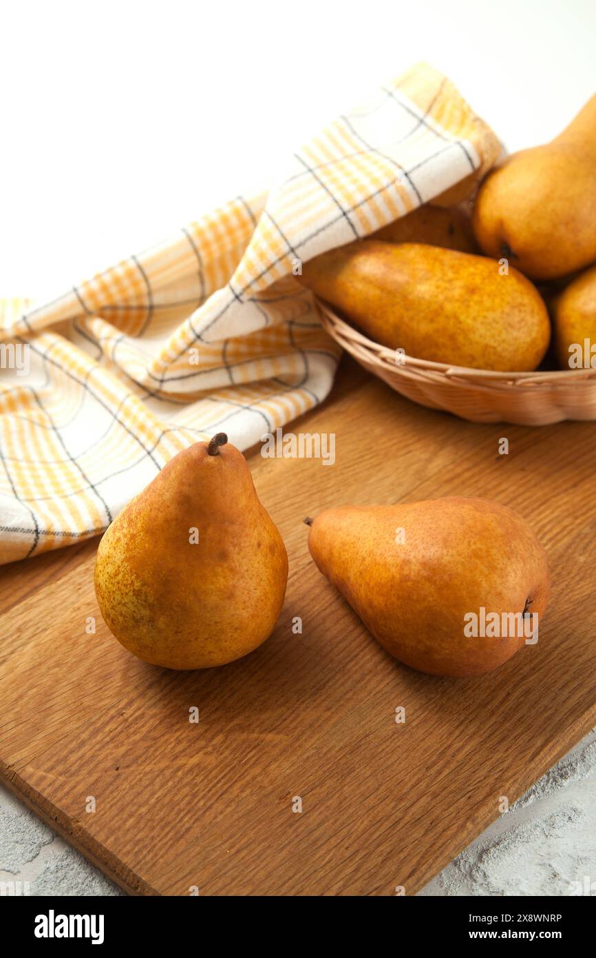 Hölzernes Schneidebrett mit Reifen saftigen Birnenfrüchten, Korb mit Birnen und gelbem Küchentuch auf weißem hölzernem Hintergrund. Stockfoto