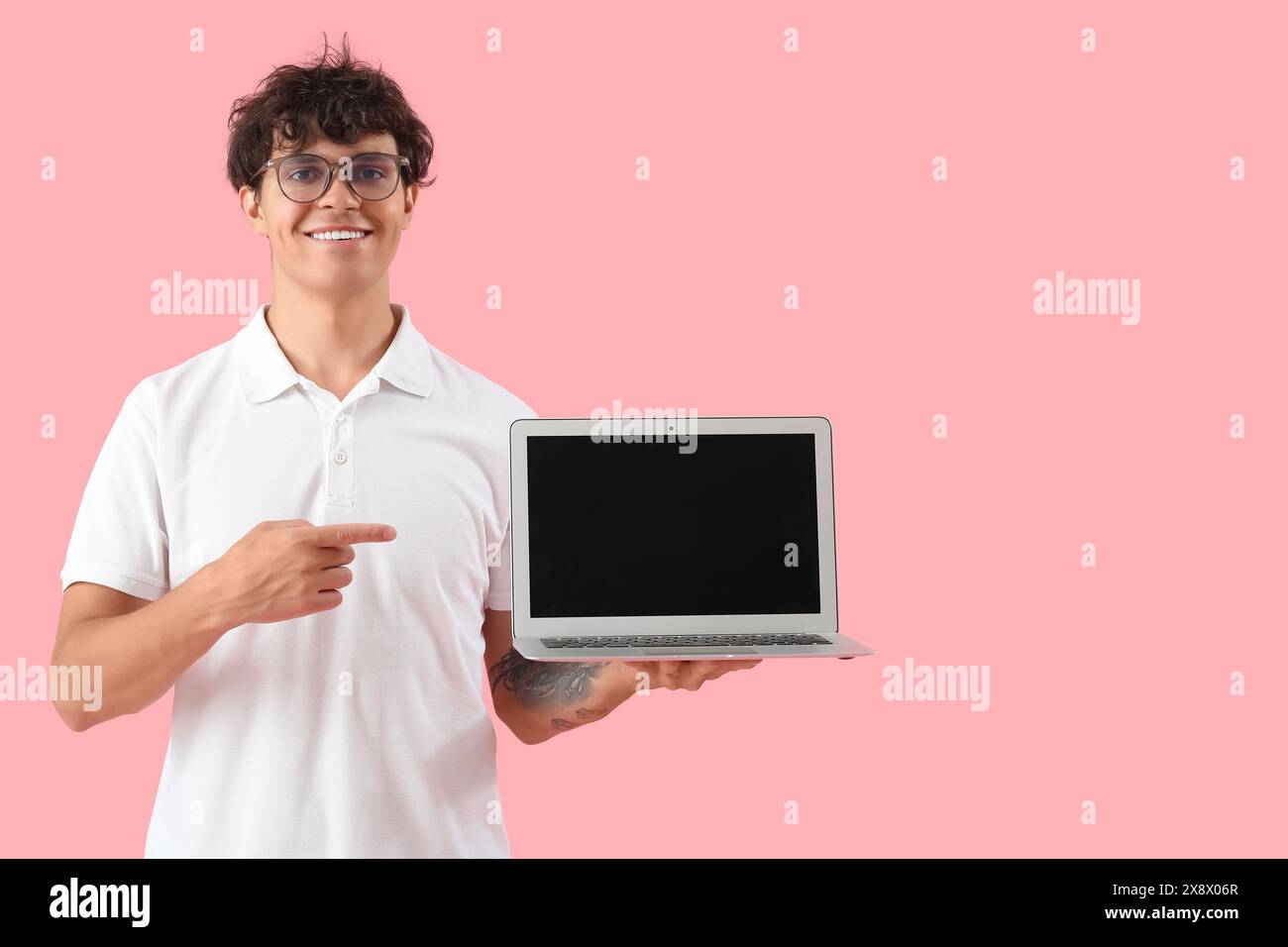Männlicher Programmierer zeigt auf leeren Laptop auf rosa Hintergrund Stockfoto