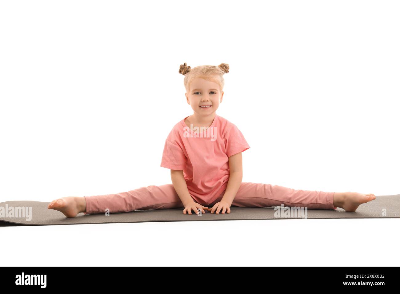 Nettes kleines glückliches Mädchen mit Matte, das Yoga auf weißem Hintergrund praktiziert Stockfoto
