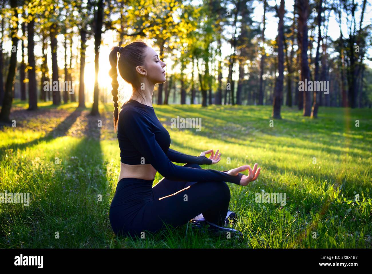 Eine junge Frau meditiert in einem ruhigen Wald bei Sonnenaufgang, umgeben von Natur Schönheit, übt Achtsamkeit Stockfoto