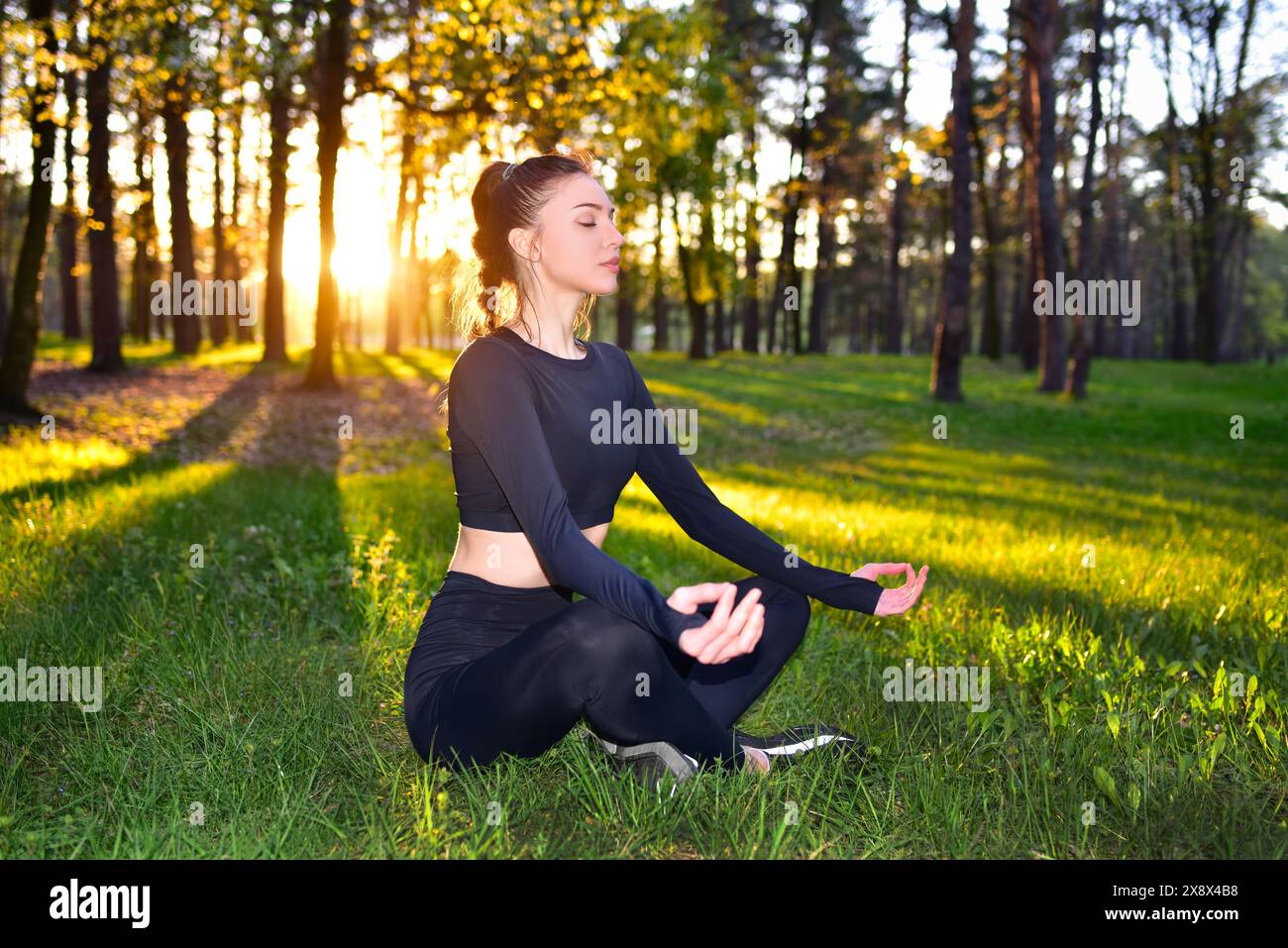 Eine Frau meditiert in einem Wald bei Sonnenuntergang, engagiert sich in Yoga und Achtsamkeit, umgeben von der Schönheit der Natur Stockfoto