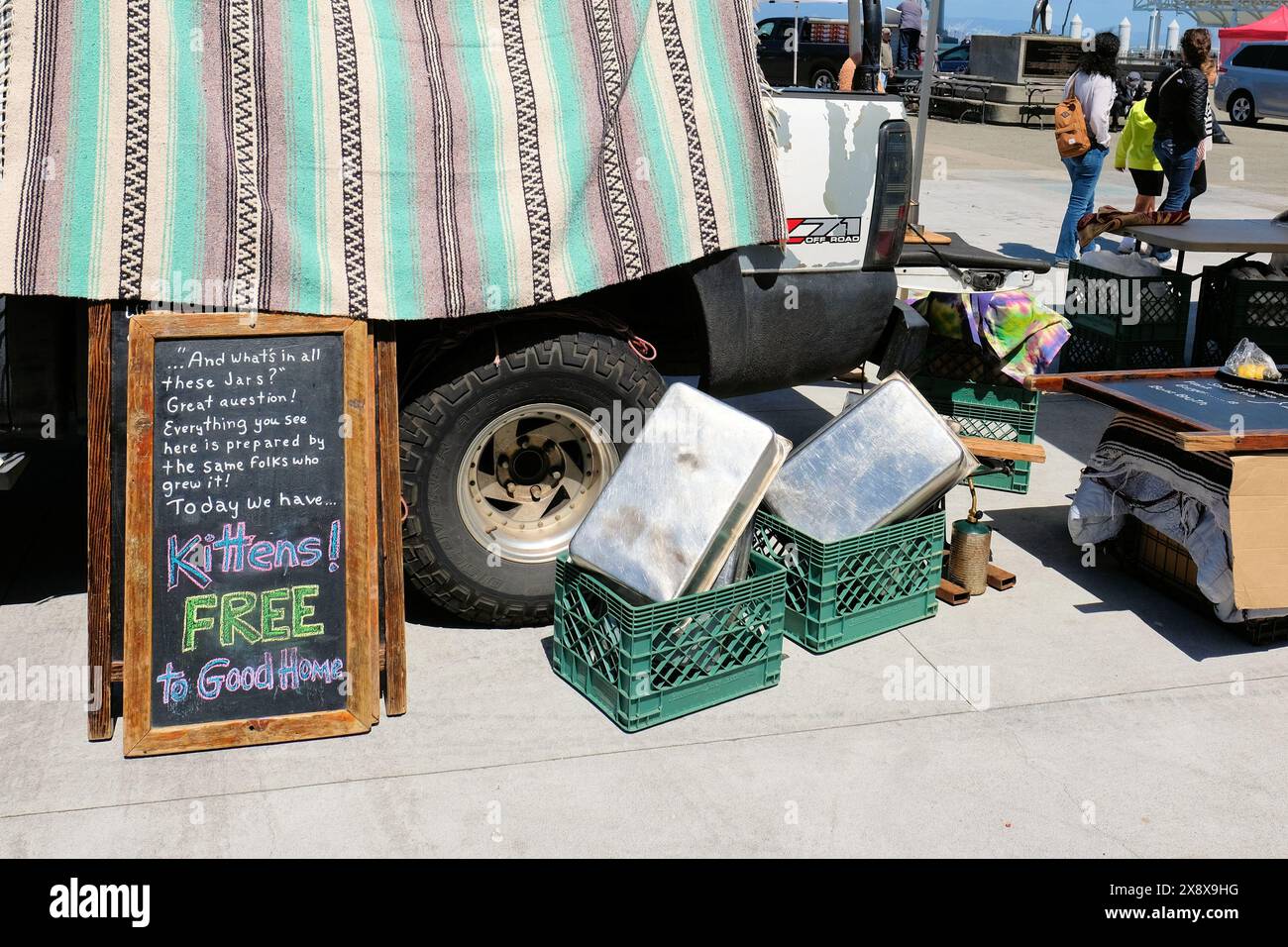 Kostenlose Kätzchen für ein Good Home-Schild neben einem Truck und Plastikkisten auf einem Bauernmarkt; Haustieradoption und Werbegeschenk für ein haustierfreundliches Zuhause. Stockfoto