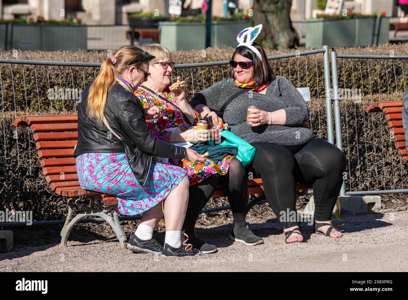 Damen mittleren Alters sitzen auf einer Bank und genießen Getränke am Maiabend im Esplanade Park. Helsinki, Finnland. Stockfoto