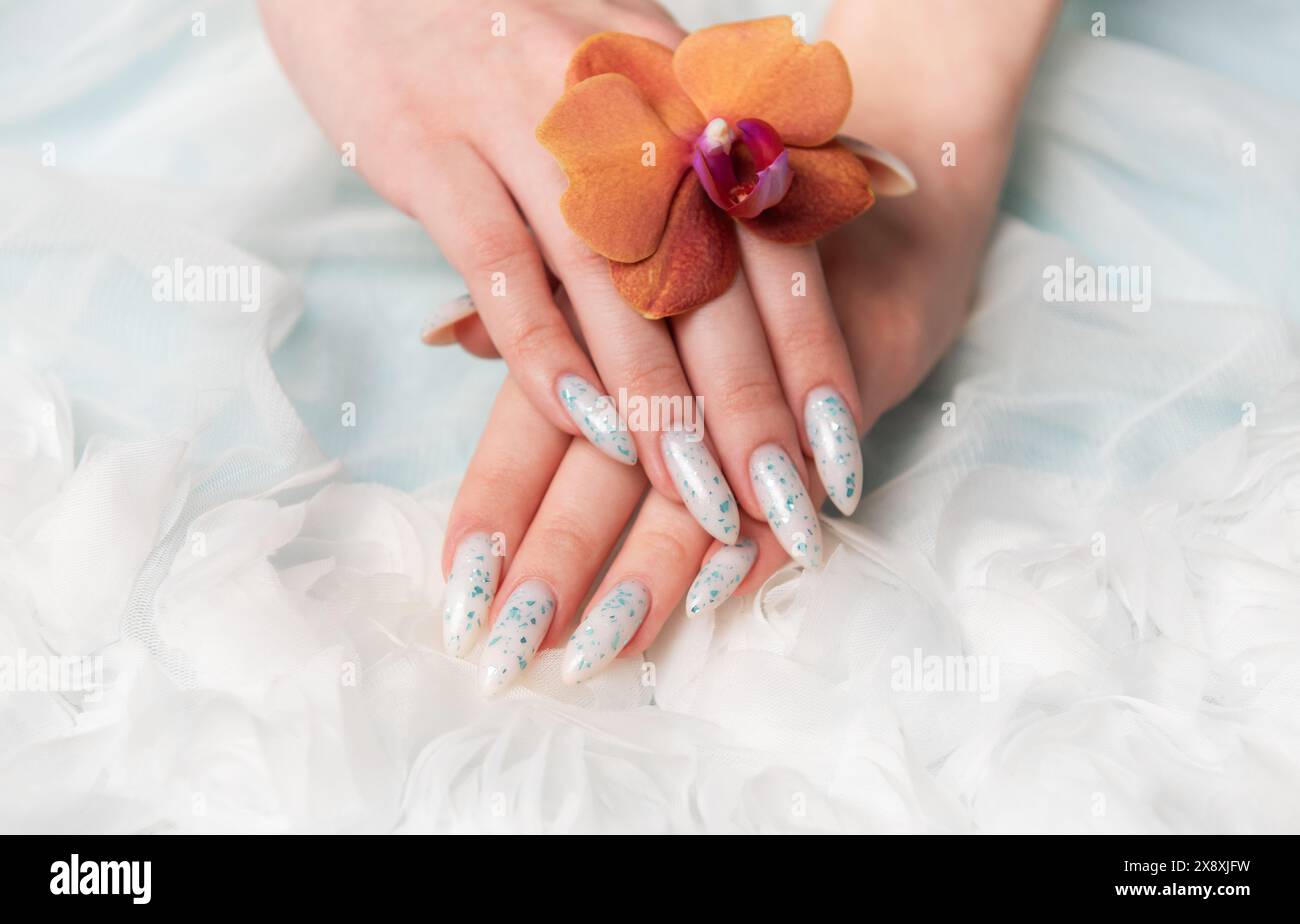 Eine Nahaufnahme zeigt eine Person Hand mit komplizierten, floralen Nailarten, die zart eine Orangenblüte umhüllt. Die umliegende weiche, schwungvolle Textur Stockfoto